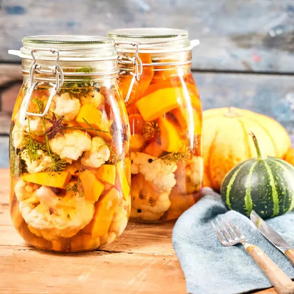 Preserving jars with pickled cauliflower and pumpkin on a wooden table