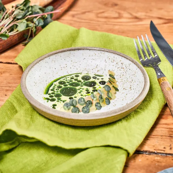Plate with green herb oil and dots of sauce, next to a green cloth