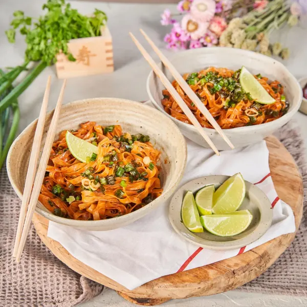 Two bowls of noodles with lime wedges and chopsticks