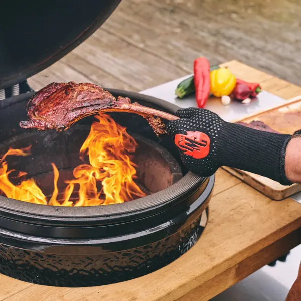 Hand in a heat glove turning meat over an open fire on a kamado
