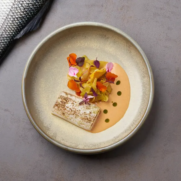 Fish fillet with vegetable garnish and sauce on a grey plate