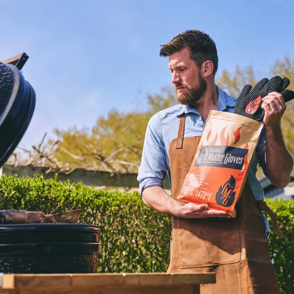 Man in an apron with the Grill Master Gloves pack in a garden