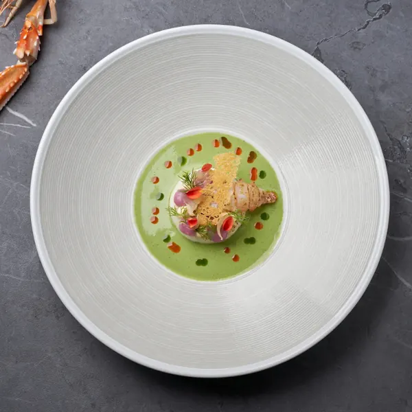 Croquette in a green soup on a white plate, seen from above