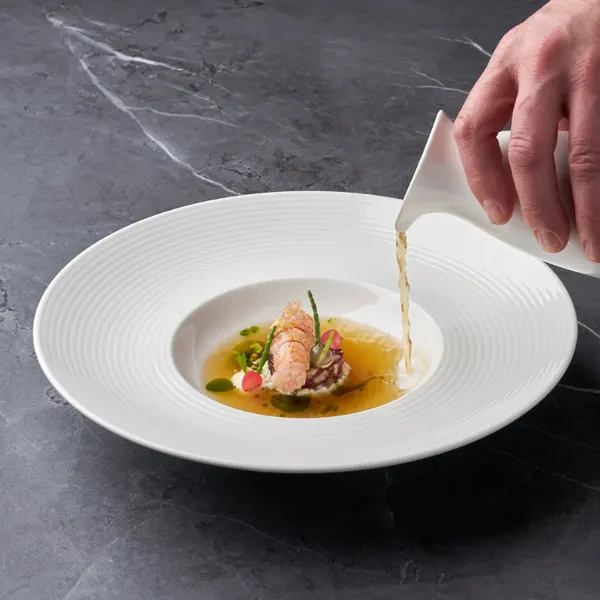 Broth being poured over a fish dish in a white deep plate