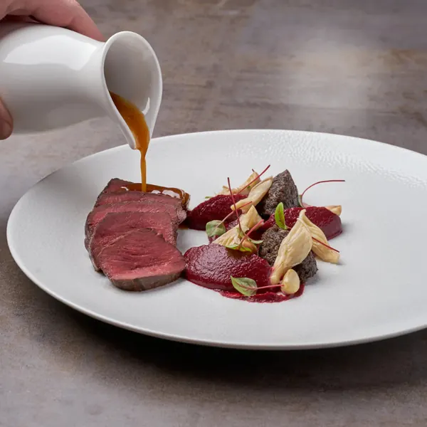Sauce being poured over sliced beef with beetroot