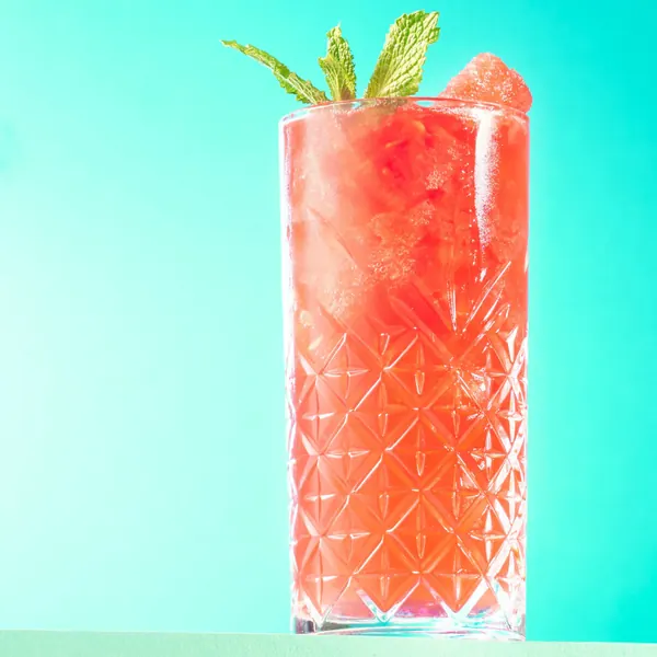 Red cocktail with mint in a cut glass against a turquoise background